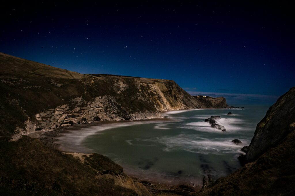 a view of a beach at night with the moon in the sky